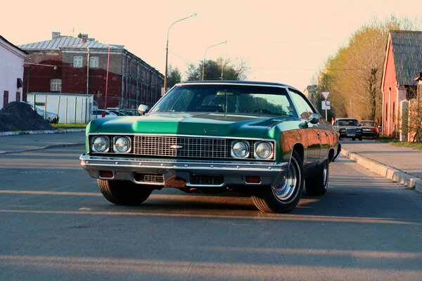 Сhevrolet impala 1973 года зелёного цвета на дороге в городке