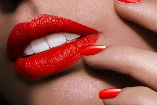 Rote Nägel, schillernde weiße Zähne auf dem Hintergrund von rotem Lippenstift