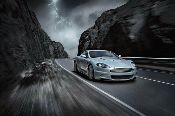 Aston martin car drives at speed on a mountain road