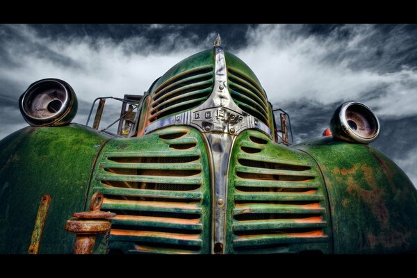 A dead green car against a cloudy sky