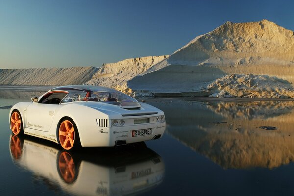 A white sports car stands on the melted ice against the background of a hill of snow and ice