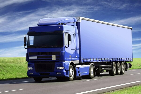 A blue truck in motion along the highway along the fields