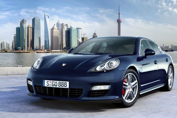 A blue Porsche stands against the backdrop of a beautiful city