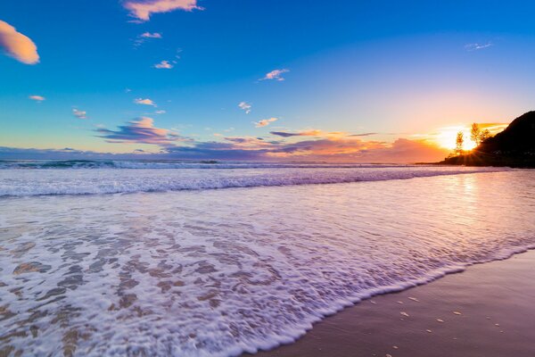Vague de mousse roulant sur le sable de la mer au coucher du soleil