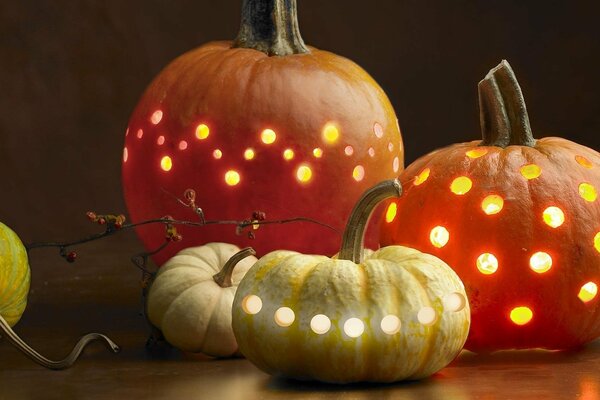 Orange and white-yellow pumpkins with lanterns inside are lying on the table