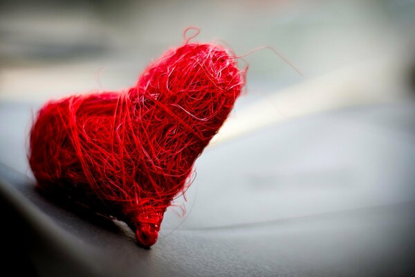 A cute heart, woven from red threads, on a gray background