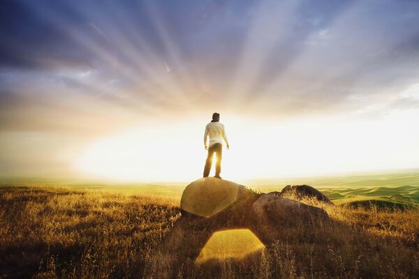 En una piedra en los rayos de la puesta de sol hay un hombre