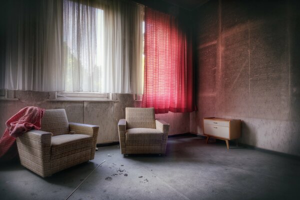 White armchairs on the concrete floor against the background of a window with a red curtain