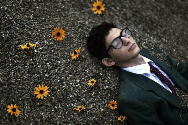 A man in a suit is lying on stones with flowers people