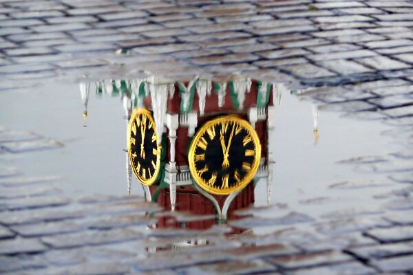 Die Reflexion der Uhr auf den Türmen des Kremls in einer Pfütze