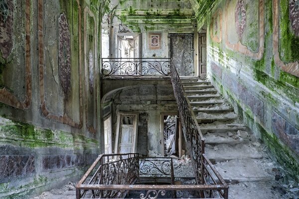 An abandoned building with moss on the walls and a staircase