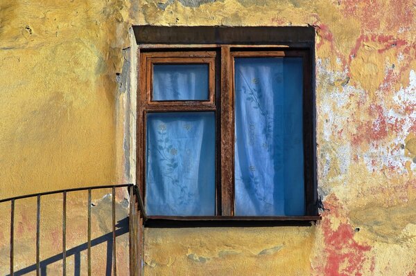 Yellow wall with a wooden window curtained with blue fabric