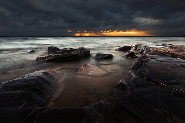 Puesta de sol oscura en la playa de piedra del mar