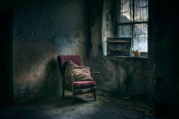 A dirty armchair with a pillow and a window with a radio