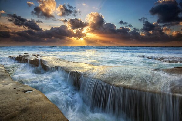 El sol detrás de las nubes, el mar y la cascada