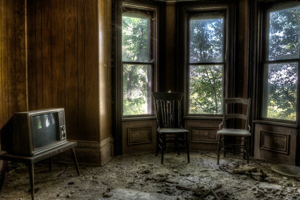 A dark room with an old TV, chairs and windows