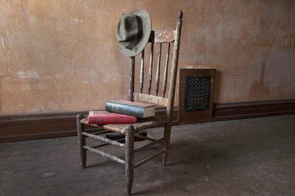Une pile de livres repose sur une chaise Vintage avec un chapeau