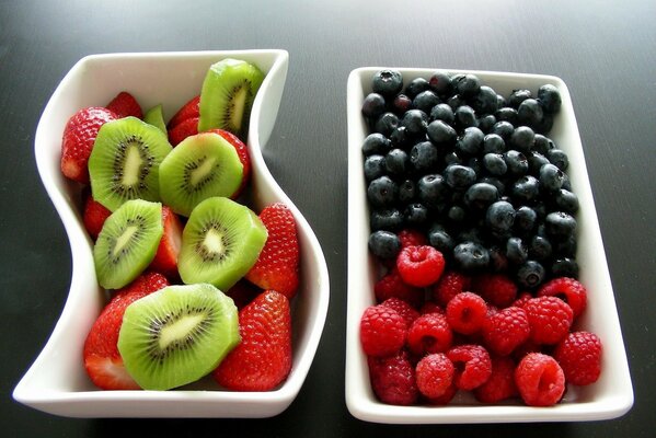 A plate with kiwi and strawberries and a plate with raspberries and blueberries