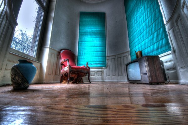 A room with an armchair, a vase and a TV