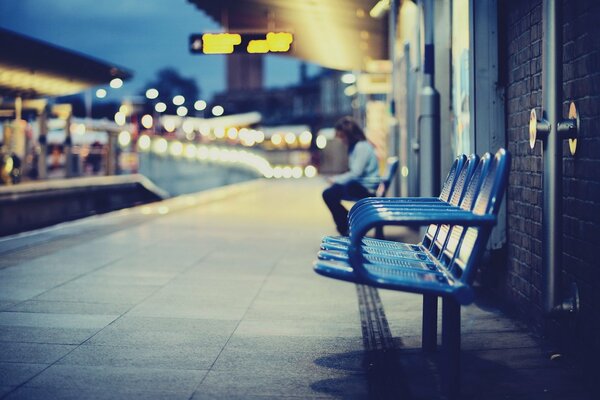 La ragazza si siede sullo strato alla sera alla stazione ferroviaria della città