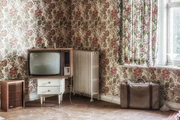 Ein Zimmer mit Blumen-Tapeten. Fernseher und Koffer