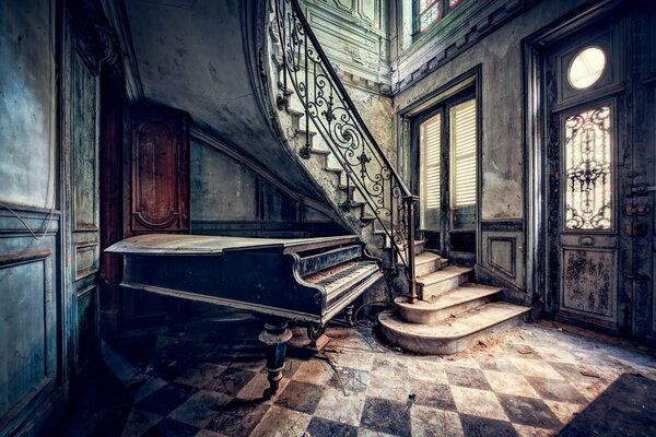 Vecchio pianoforte a coda sotto le scale in una vecchia casa