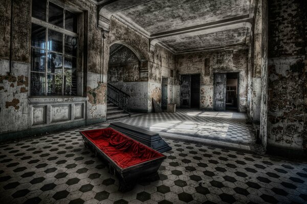 Ein offener Sarg, der mit rotem Seidentuch umhüllt ist, steht auf dem Boden eines alten, verlassenen Raumes