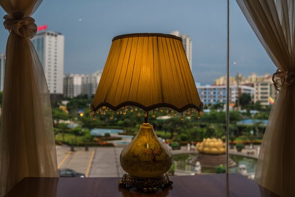 A lamp on the table by the window with a beautiful view of the city