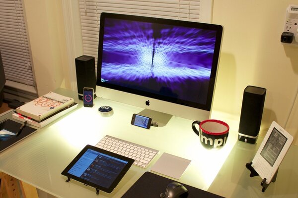 There is a book, a phone, a gadget on the table and there is a monitor