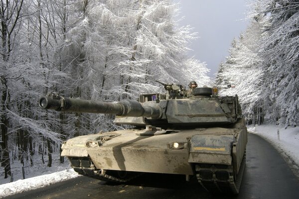 El tanque monta en el camino entre el bosque cubierto de nieve