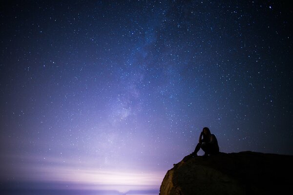 Chica en una roca en la noche contra el cielo estrellado