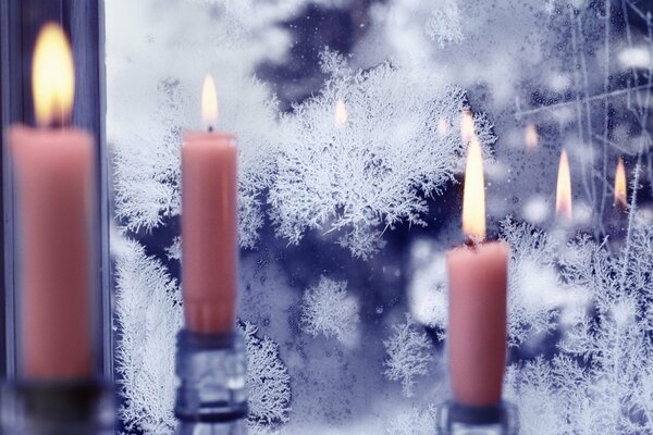 A burning pink candle is reflected in a frozen window