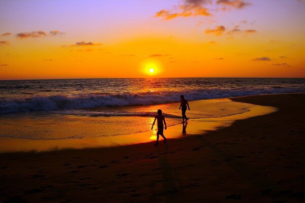 People walk along the seashore at sunset