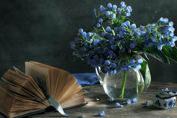 Stillleben von blauen Blumen in einer Vase mit einem alten Buch