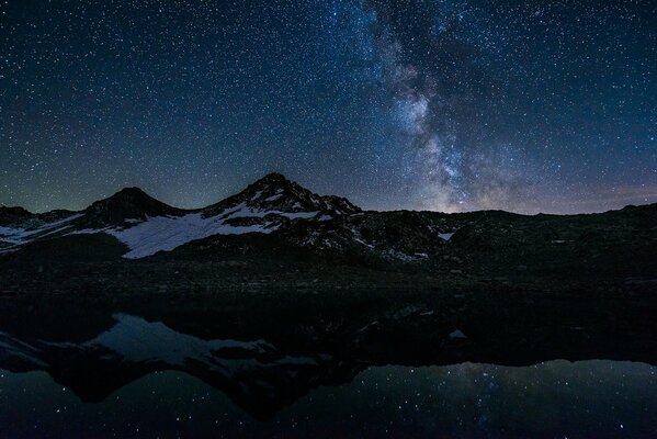 Réflexion des étoiles dans le lac de nuit avec des montagnes enneigées
