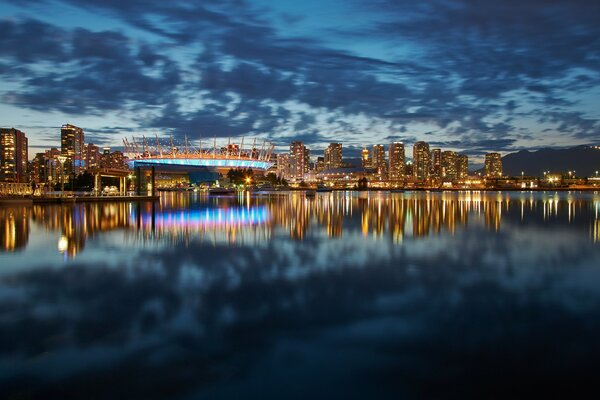 The evening city on the shore of the bay is reflected in the water