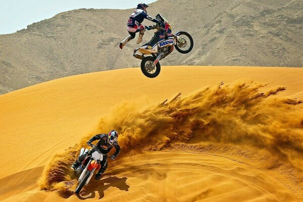 Two motorcyclists jump on motorcycles in the desert