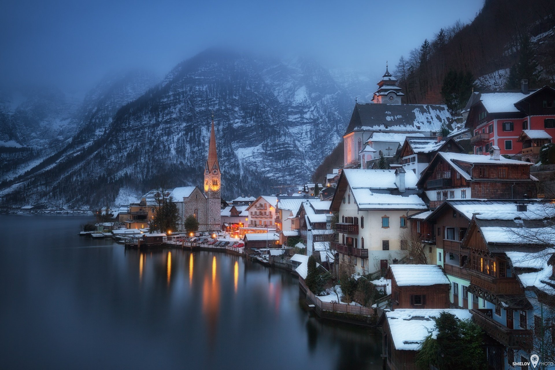 austria città comune hallstatt salzkammergut inverno neve montagne alpi lago riva case luci foschia