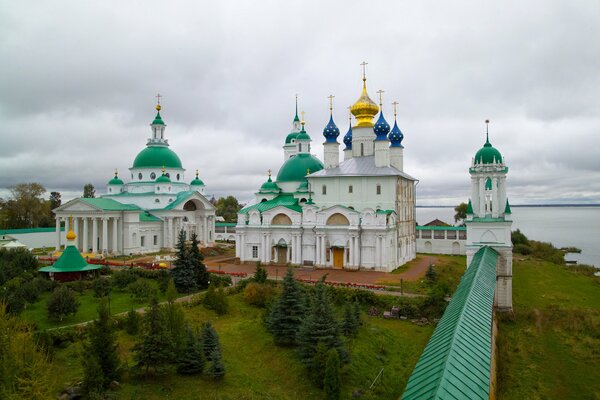 White cathedral with green, blue domes on the shore