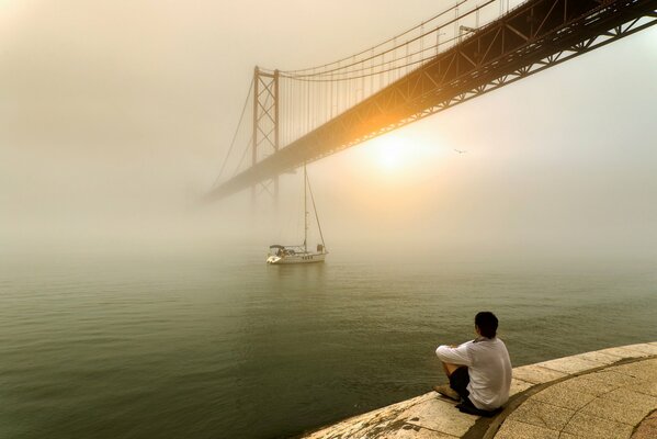 A man looks at the sunrise over the fog and the bridge