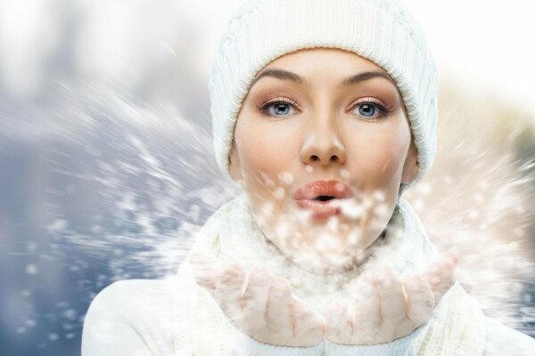 Das Mädchen bläst im Winter den Schnee aus den Händen