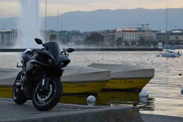 Moto Yamaha nera sul lungomare. Fontana. Barche al molo