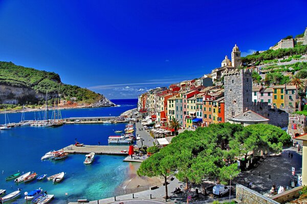 Trees, boats and houses on the embankment against the background of the blue sea