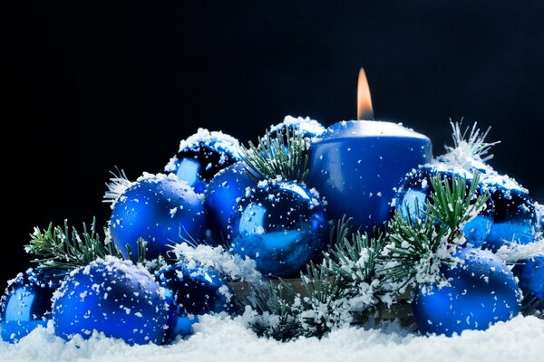 A burning candle in the snow with Christmas tree toys