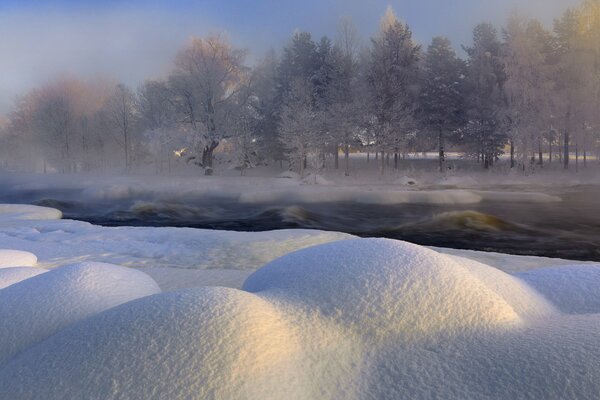 Paesaggio invernale, cumuli di neve sulla riva del fiume, foresta