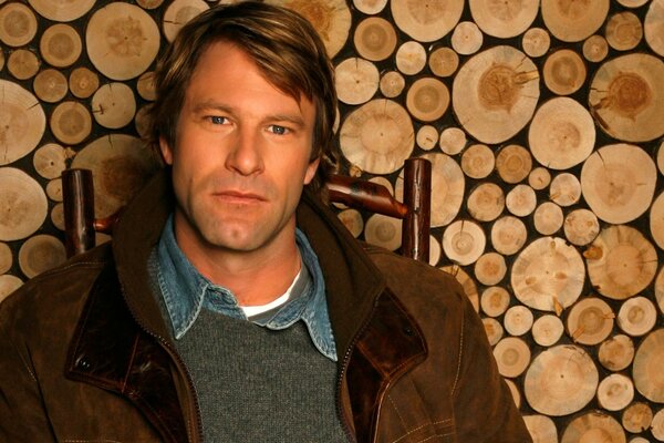 Aaron Eckhart on a chair in a brown jacket