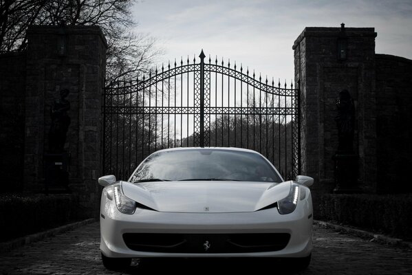 Ferrari blanco de pie frente a la puerta forjada