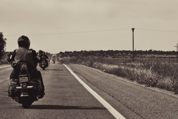 A motorcyclist rides a bike into the distance in a vintage photo