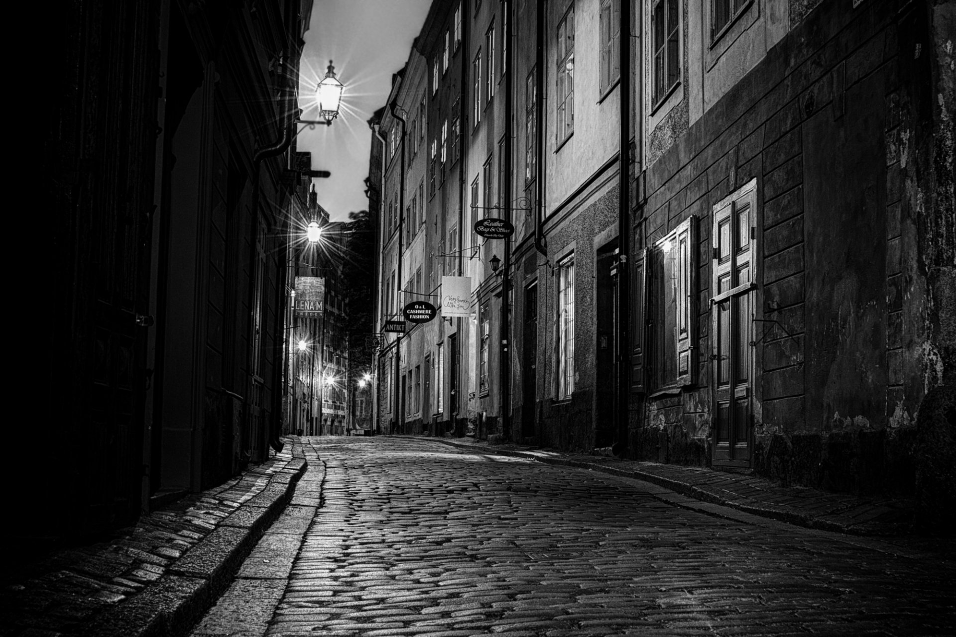 weden city night street paving stones road shops buildings houses doors windows lights black and white