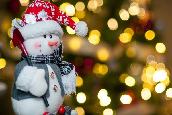 Muñeco de nieve de juguete con pala delante del árbol de Navidad